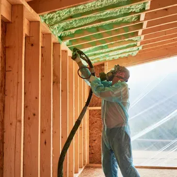 Person in protective suit spraying insulation foam on a ceiling.