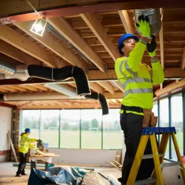 Person in protective suit spraying insulation foam on a ceiling.