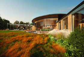 Modern wooden building with large windows and a curved roof, surrounded by grassy fields and a pool.