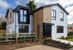 Modern two-story house with white walls, wood accents, black trim, and a small garden in front.