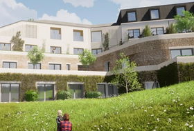 Multi-story building with green roof and exterior, grassy hill. Two people stand in foreground.