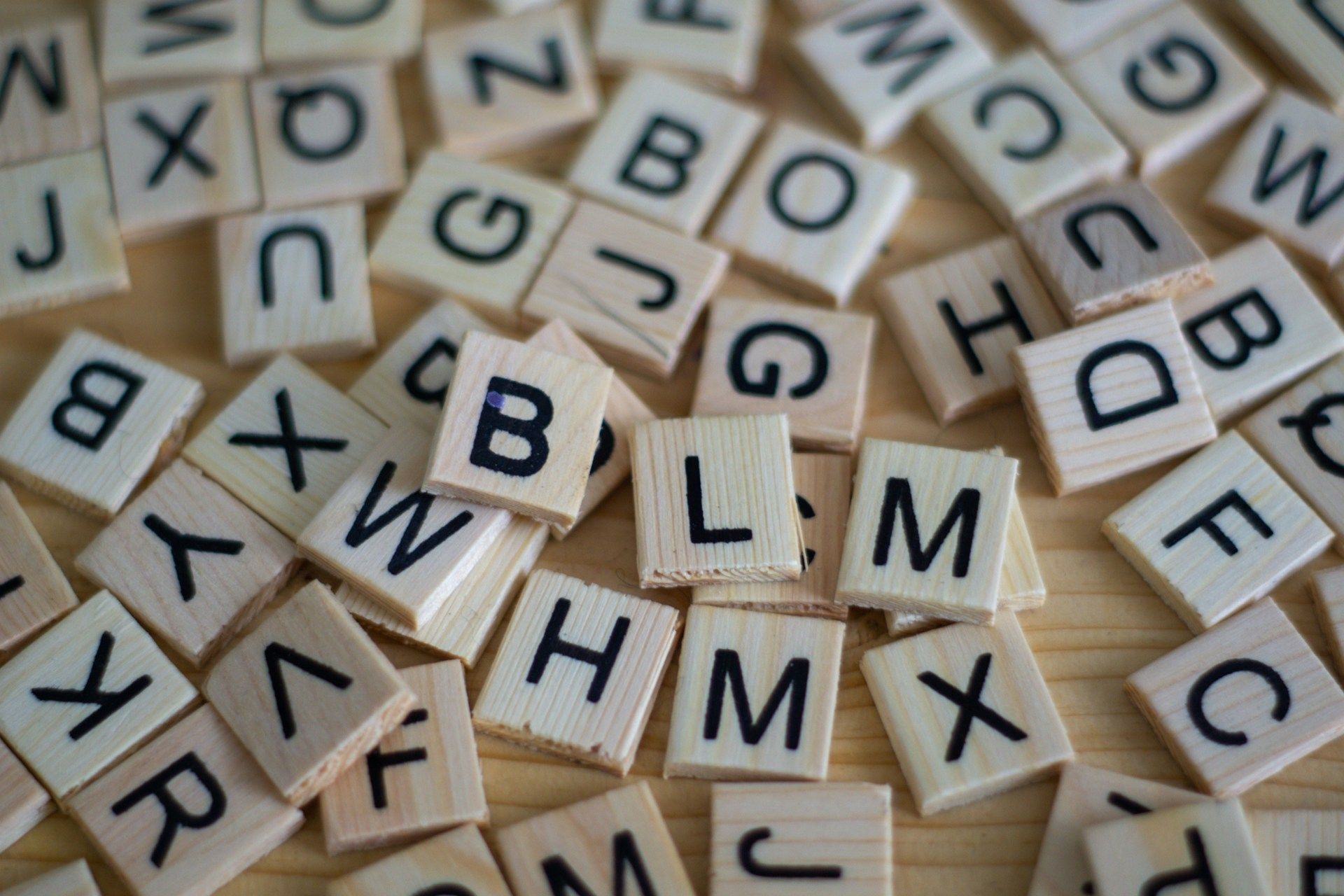 Scattered wooden letter tiles spelling words on a tabletop, with several tiles stacked and overlapping.