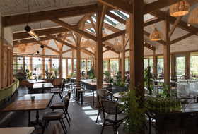 Bright, airy restaurant interior with wooden beams, tables, chairs, plants, and natural light.