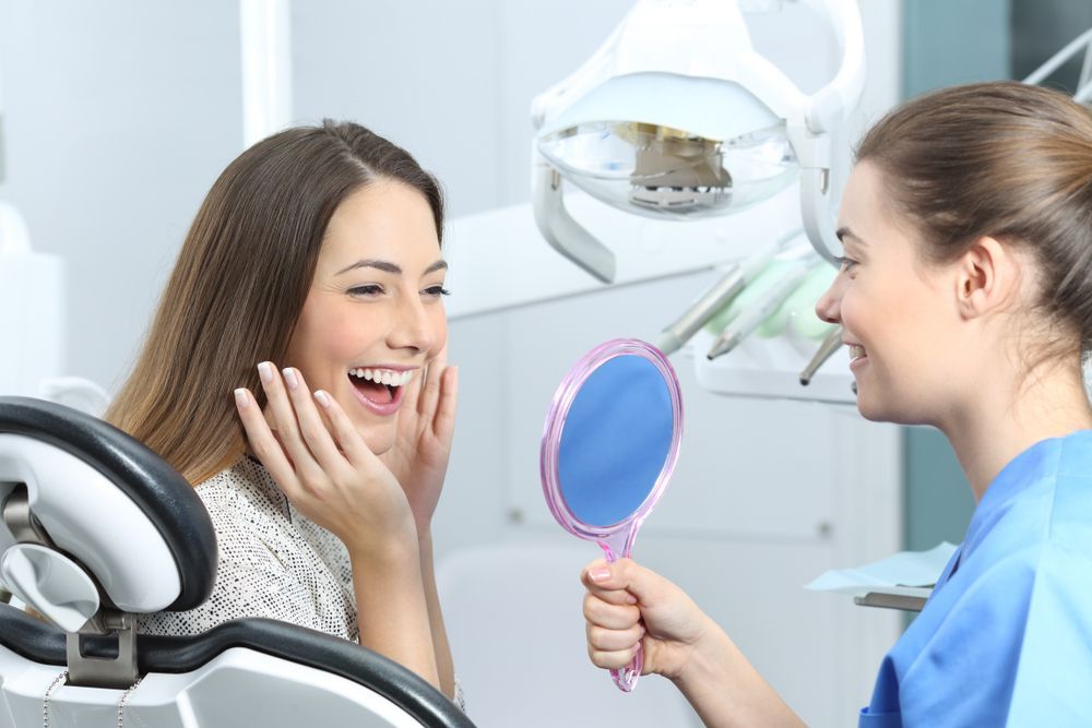 A Woman Is Looking At Her Smile In A Mirror At The Dentist — Alice Denture Clinic In Ciccone, NT