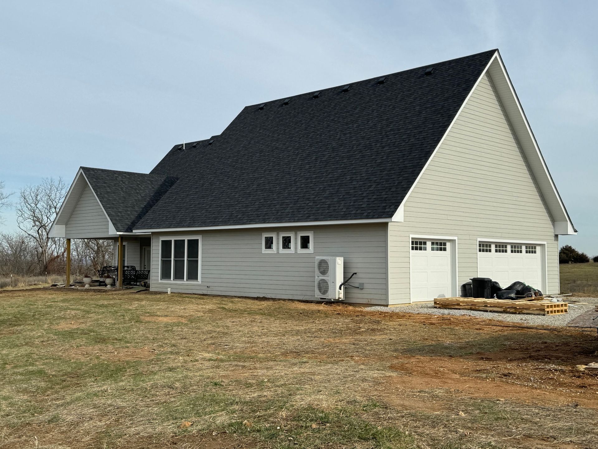 A white house with a black roof is sitting in the middle of a field.