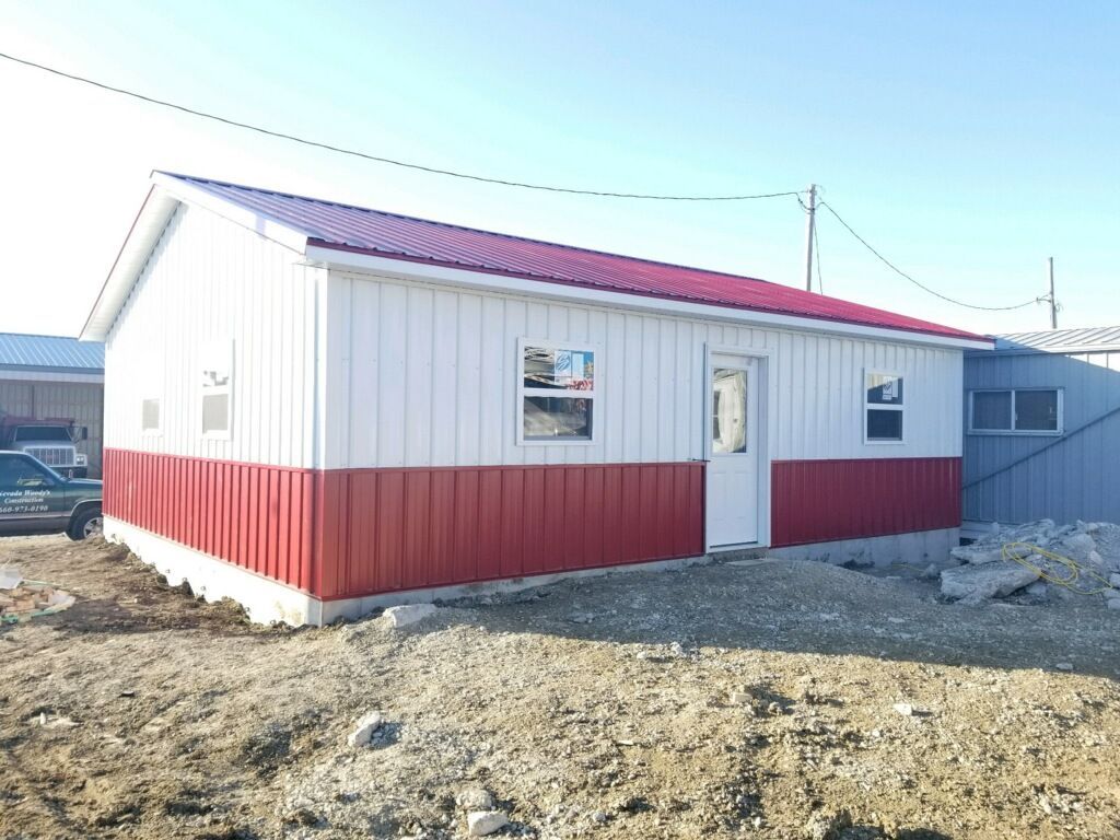A small red and white building with a red roof is sitting in the middle of a dirt field.