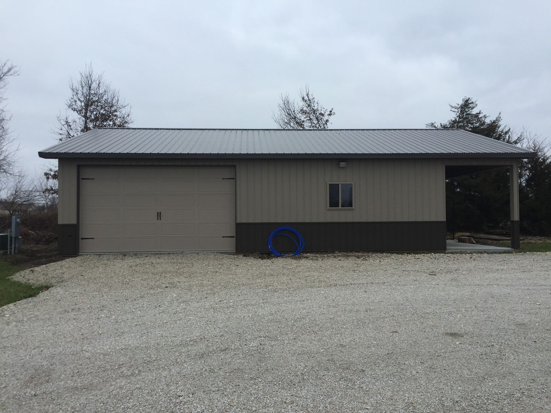 A garage with a gray roof is sitting on top of a gravel driveway.