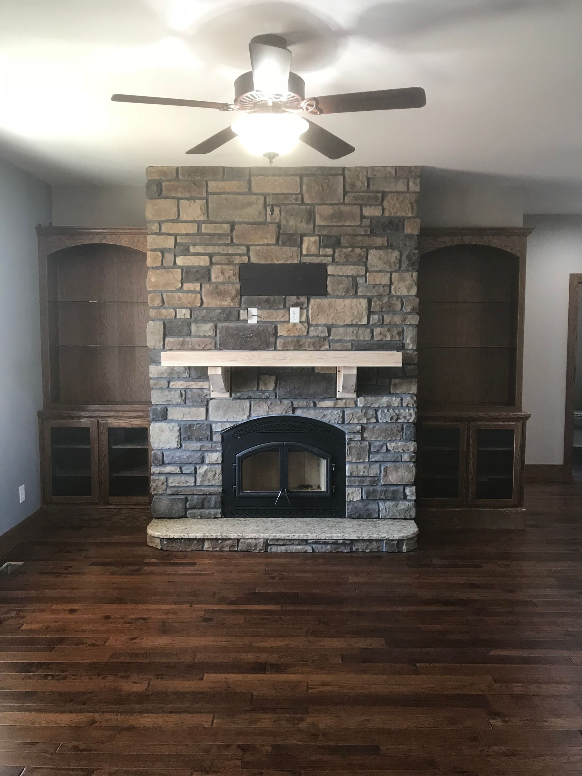 A living room with a stone fireplace and a ceiling fan.