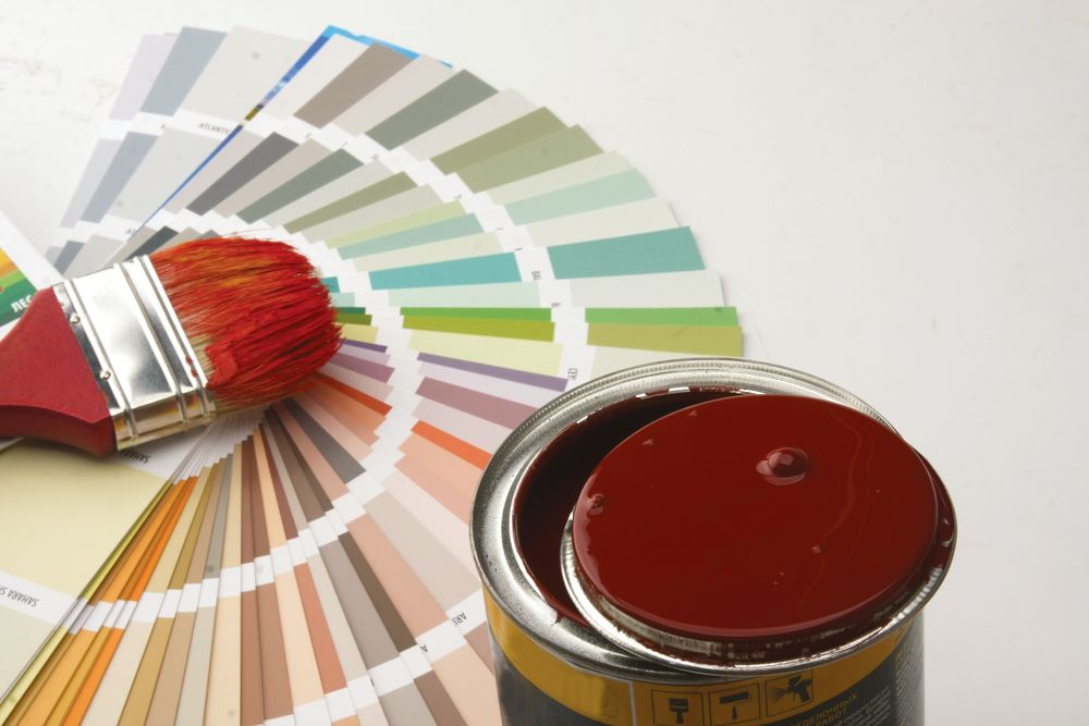 A hand with a paint roller painting a white surface dark grey