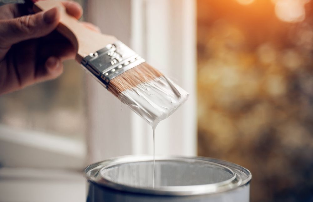 A painter in a bright yellow shirt painting the outside of a building a dark grey