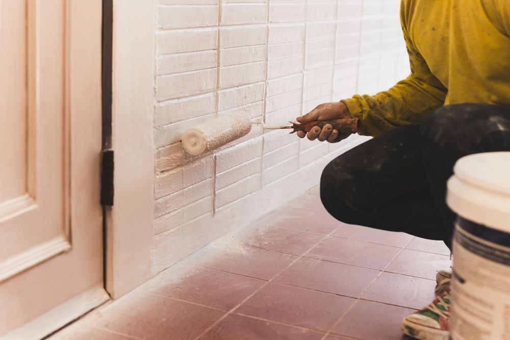 A hand with a paint roller painting a white surface dark grey