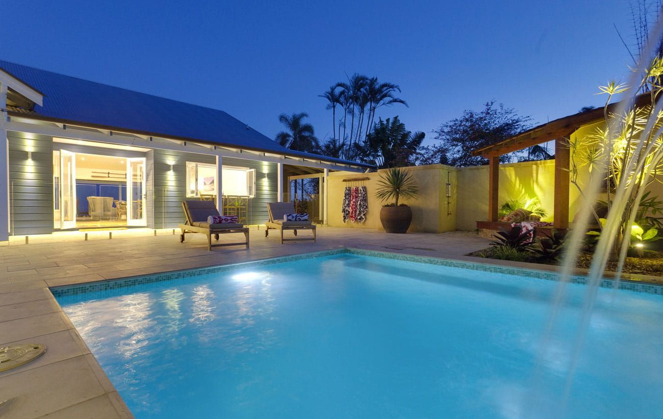 A Large Swimming Pool With a Waterfall in the Backyard of a House — Sigley Electrical in Mooball, NSW