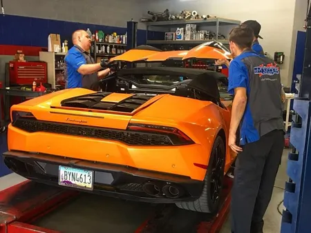 Two mechanics working on an orange Car convertible in a repair shop. | Dyno-Comp