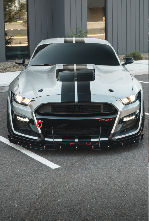 Silver Ford Mustang Shelby with black stripes, modified front bumper, parked outdoors. | Dyno-Comp