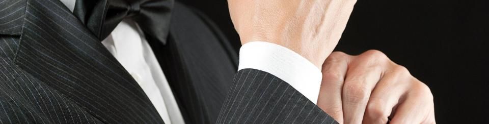 A person wearing a pinstripe tuxedo, white dress shirt, and black bowtie, shown from the chest up against a black background.