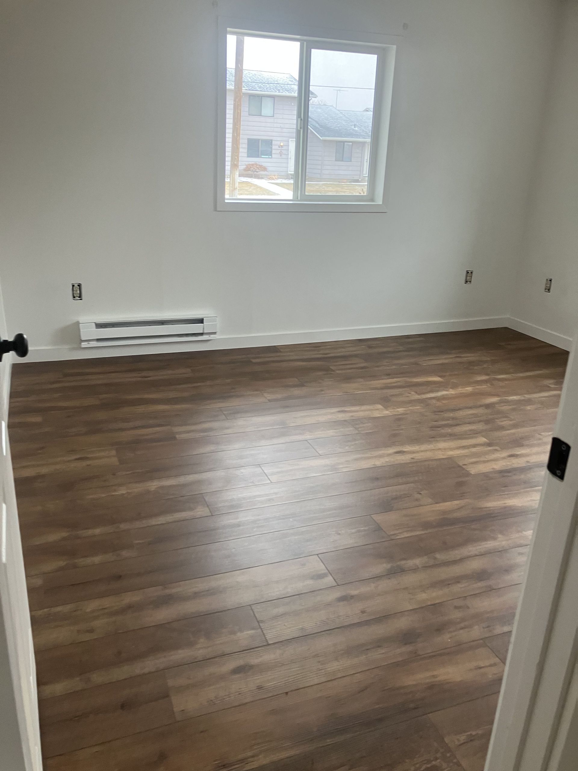Plumber in plaid shirt uses a wrench under a bathroom sink.