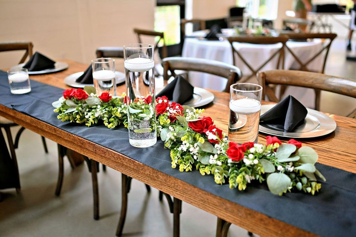 Wedding reception table with floral garland, candles, and black napkins.