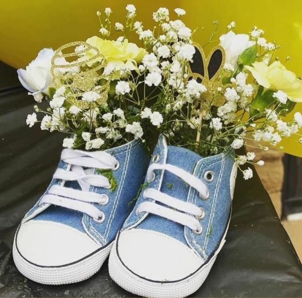 Blue denim baby shoes filled with white and yellow flowers, party decor.