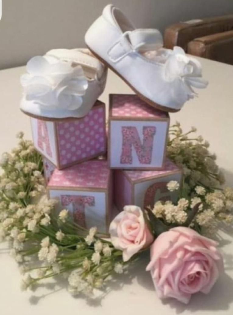 Baby shoes atop stacked letter blocks spelling surrounded by flowers.