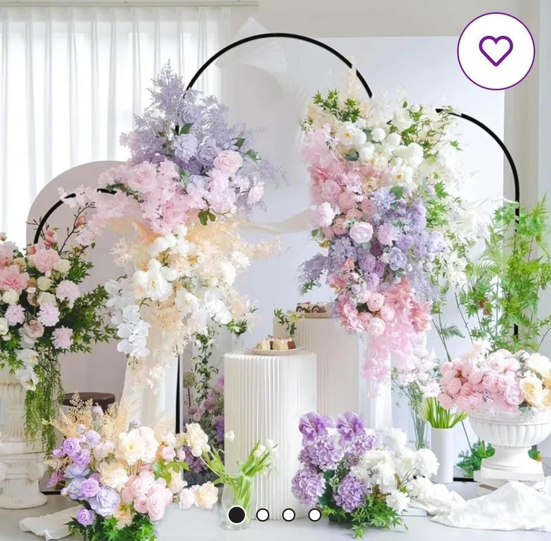 Floral arrangement backdrop with white, pink, and purple flowers; black arches; and white pedestals.
