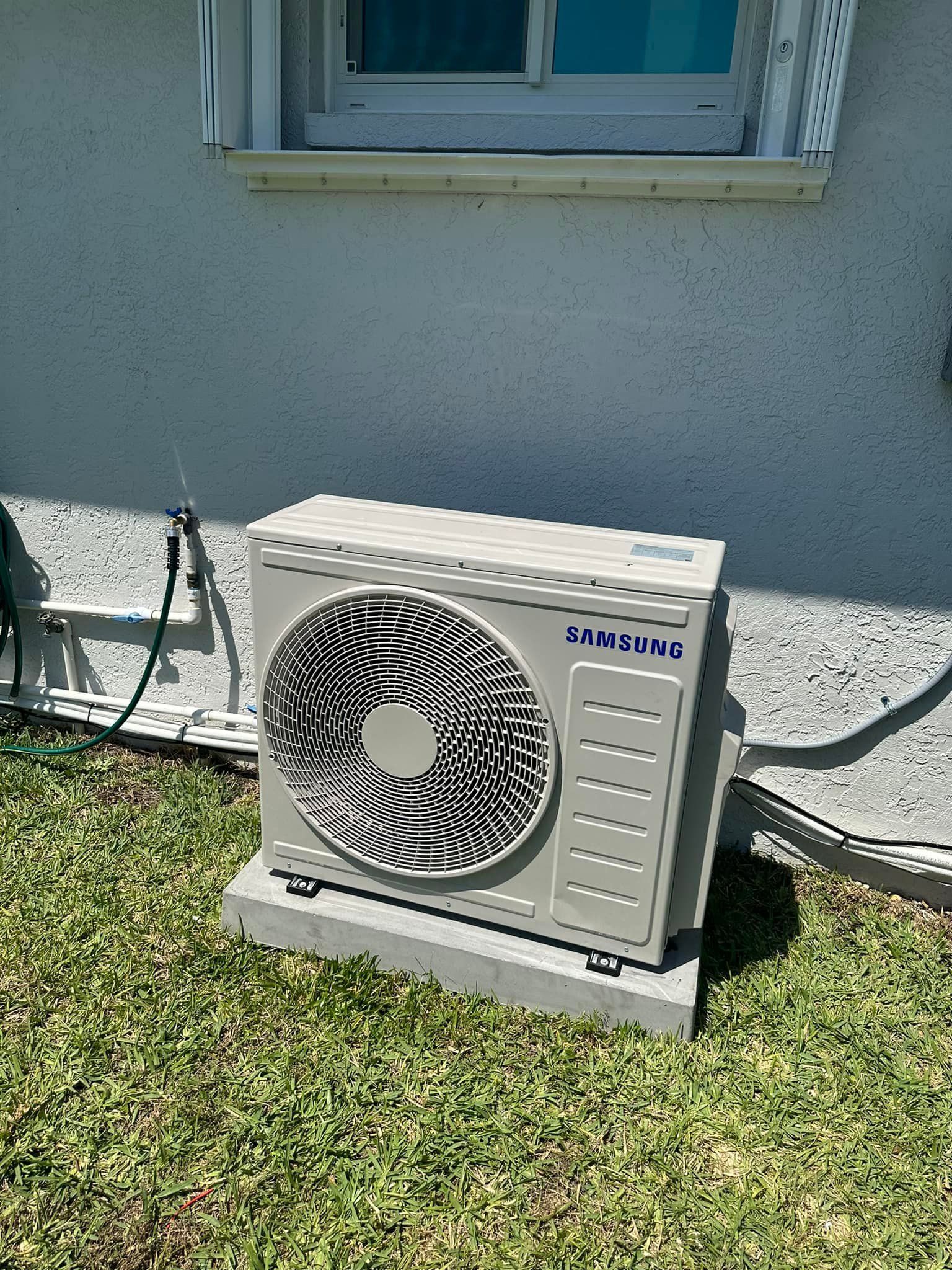 Air conditioner unit on a concrete base, outside a building, near a window.