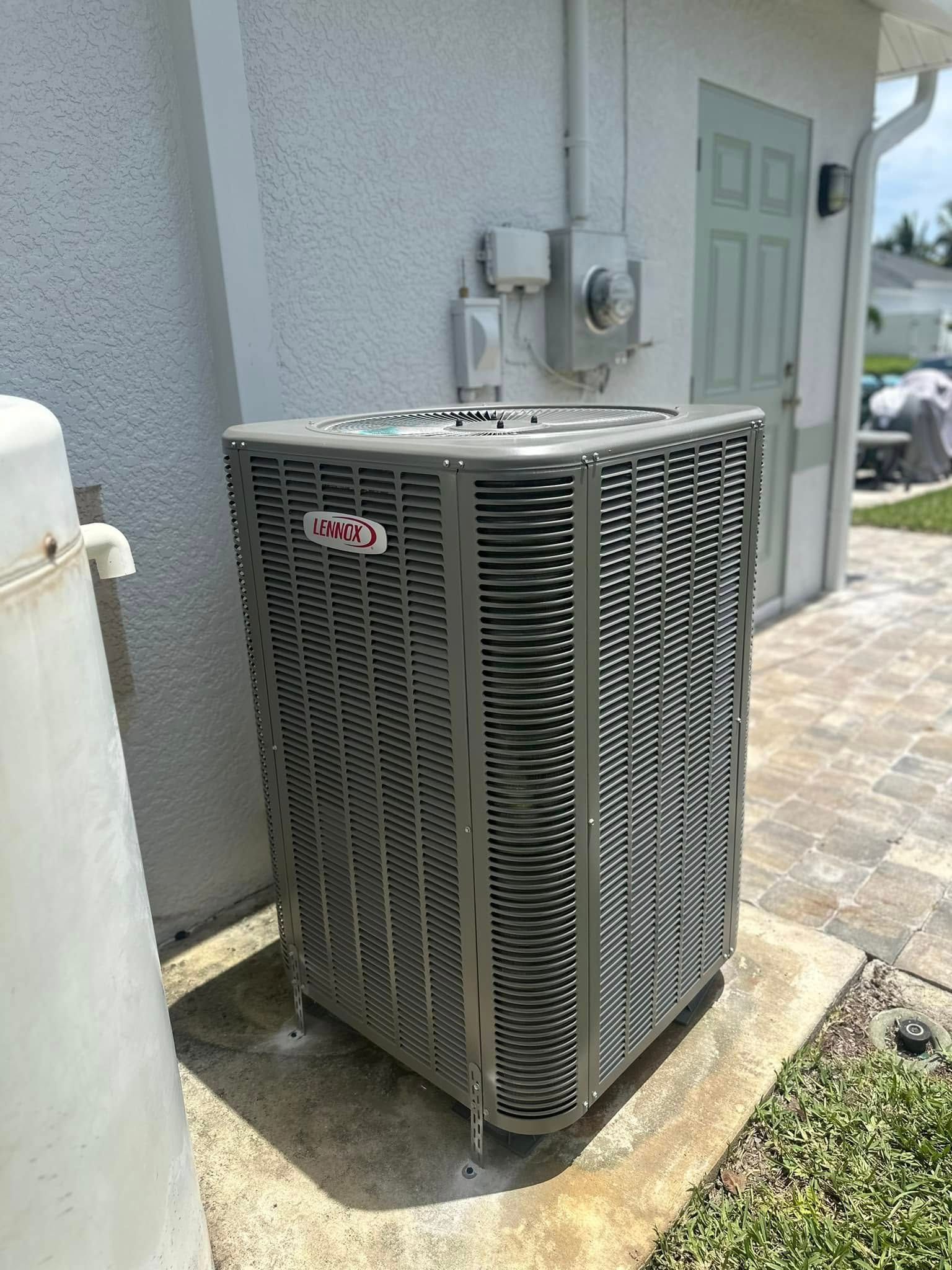 Air conditioning unit next to a white wall and a small door, outdoors.