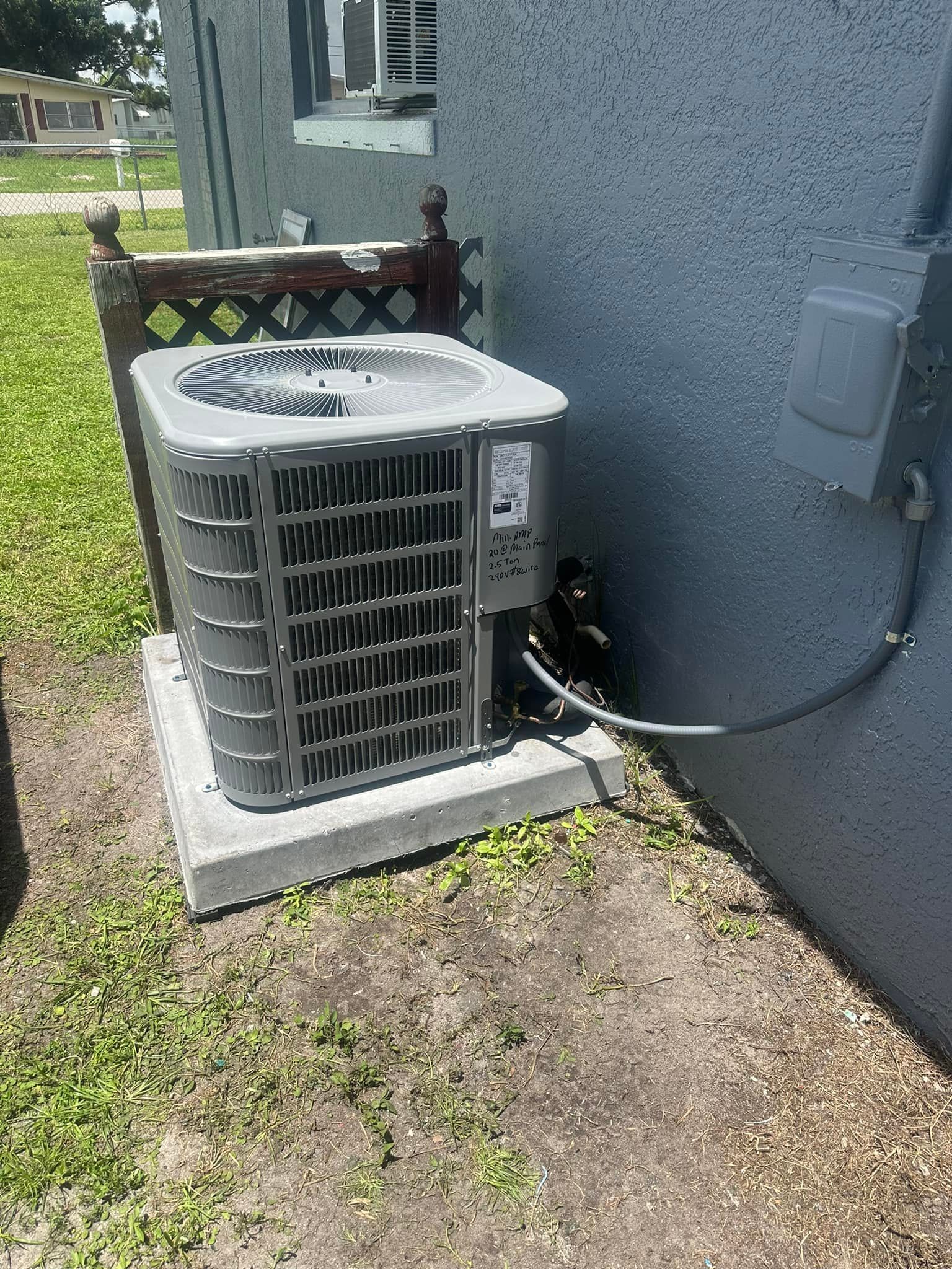 Air conditioning unit on a concrete pad next to a gray building.