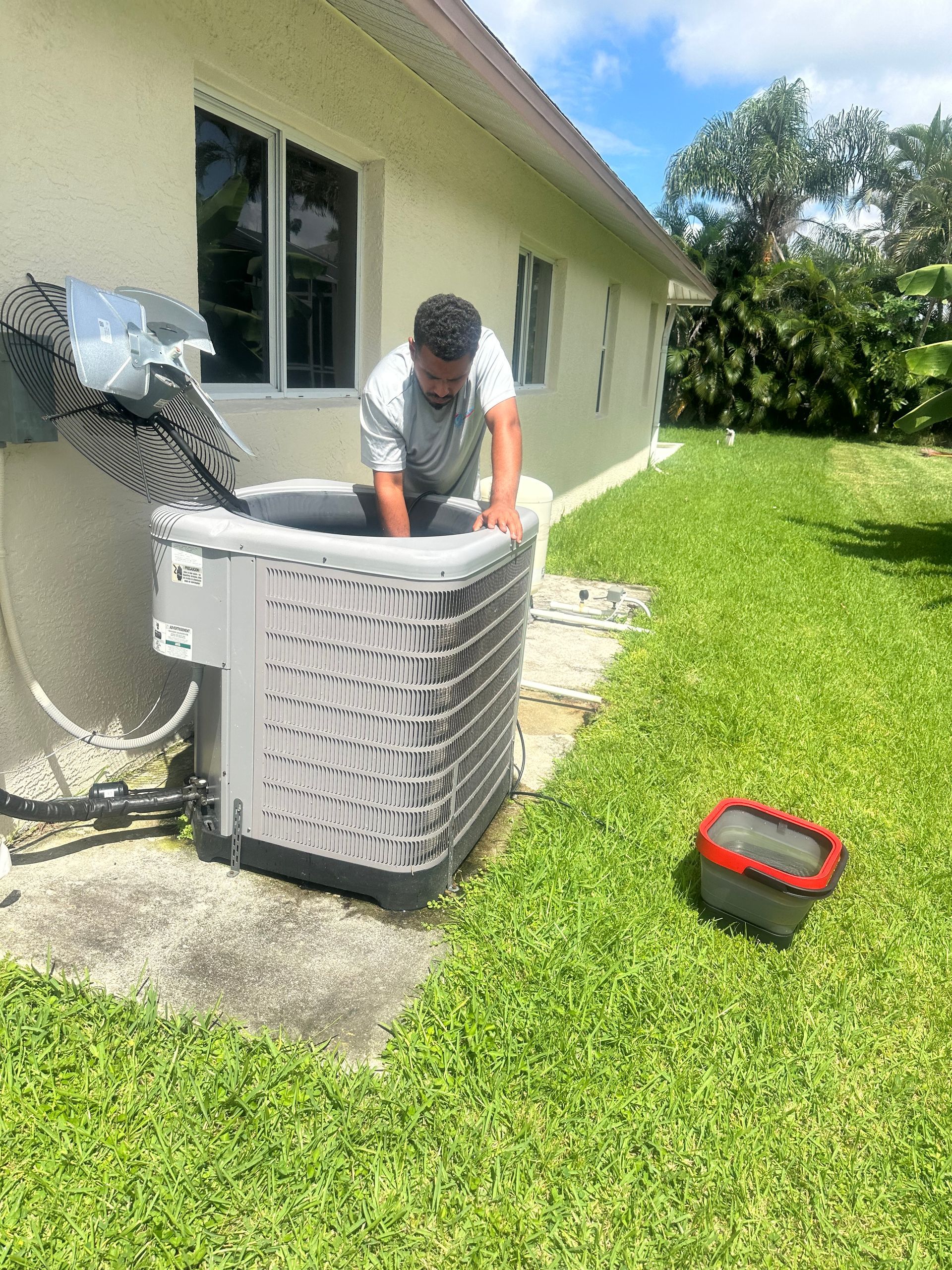 Man working on an AC unit outdoors next to a house on a sunny day.