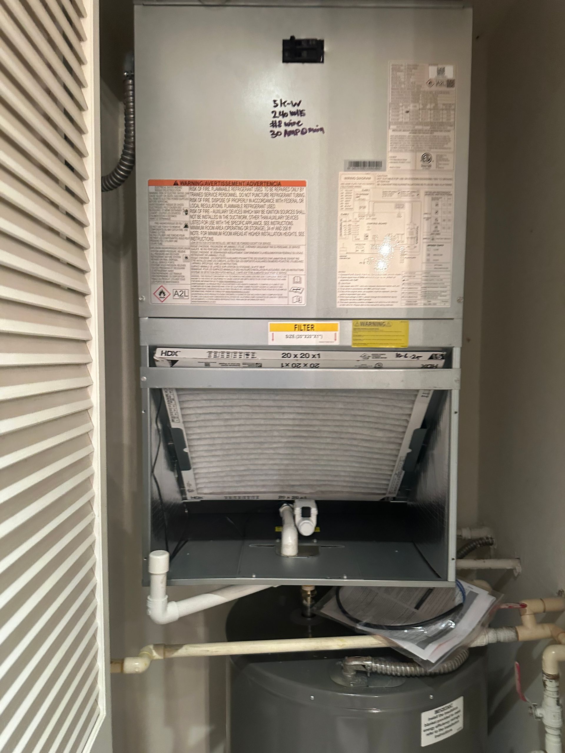 Furnace with open filter door, next to a water heater in a utility closet.