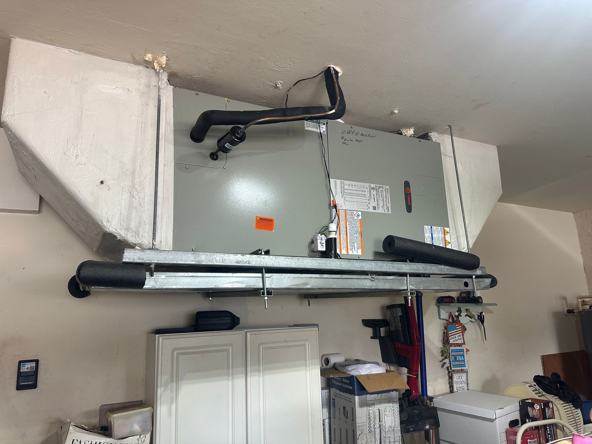 HVAC unit mounted on a garage ceiling with ductwork and cabinet below.