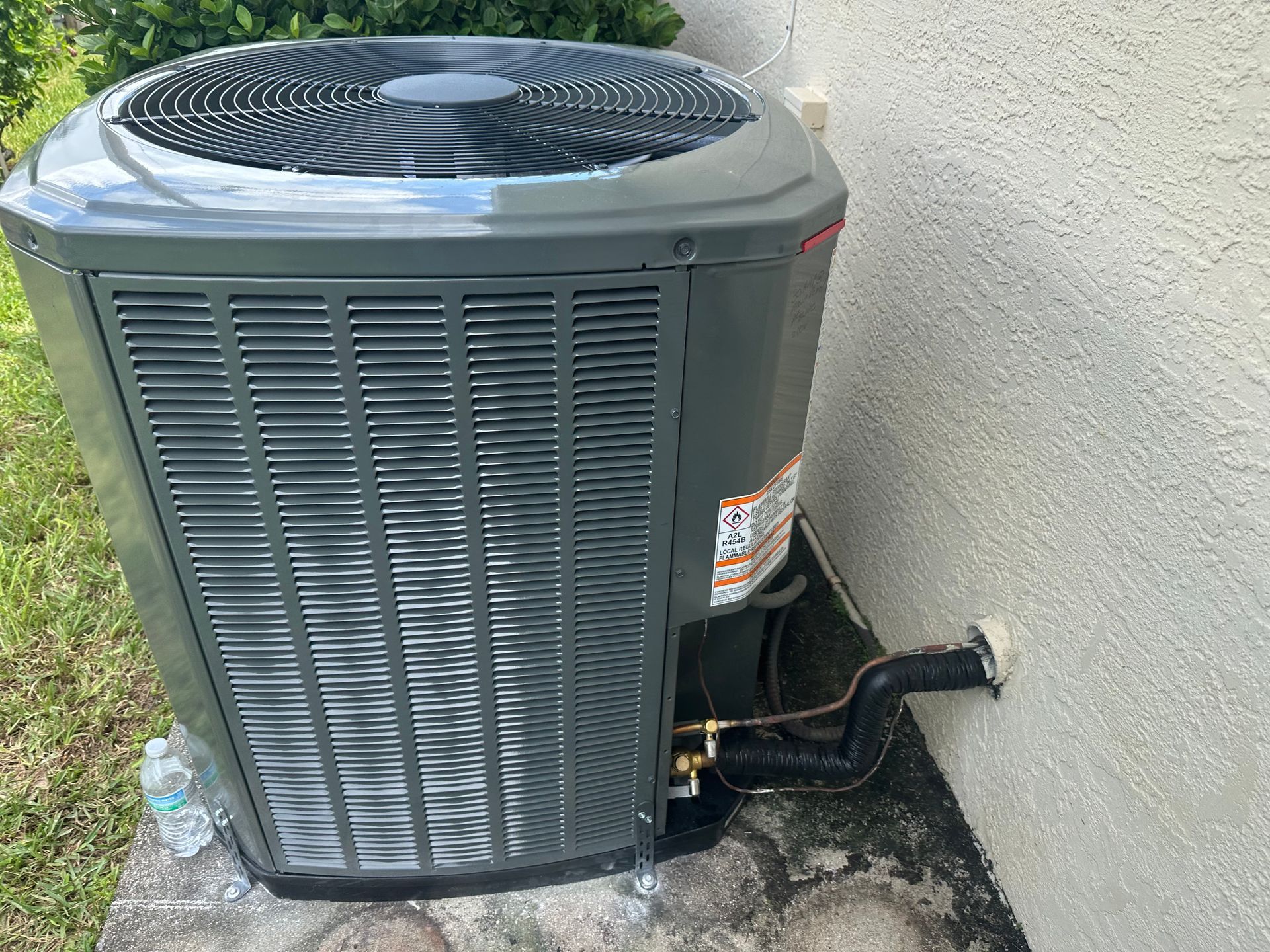 Gray air conditioning unit outside a light stucco building, sitting on a concrete pad.