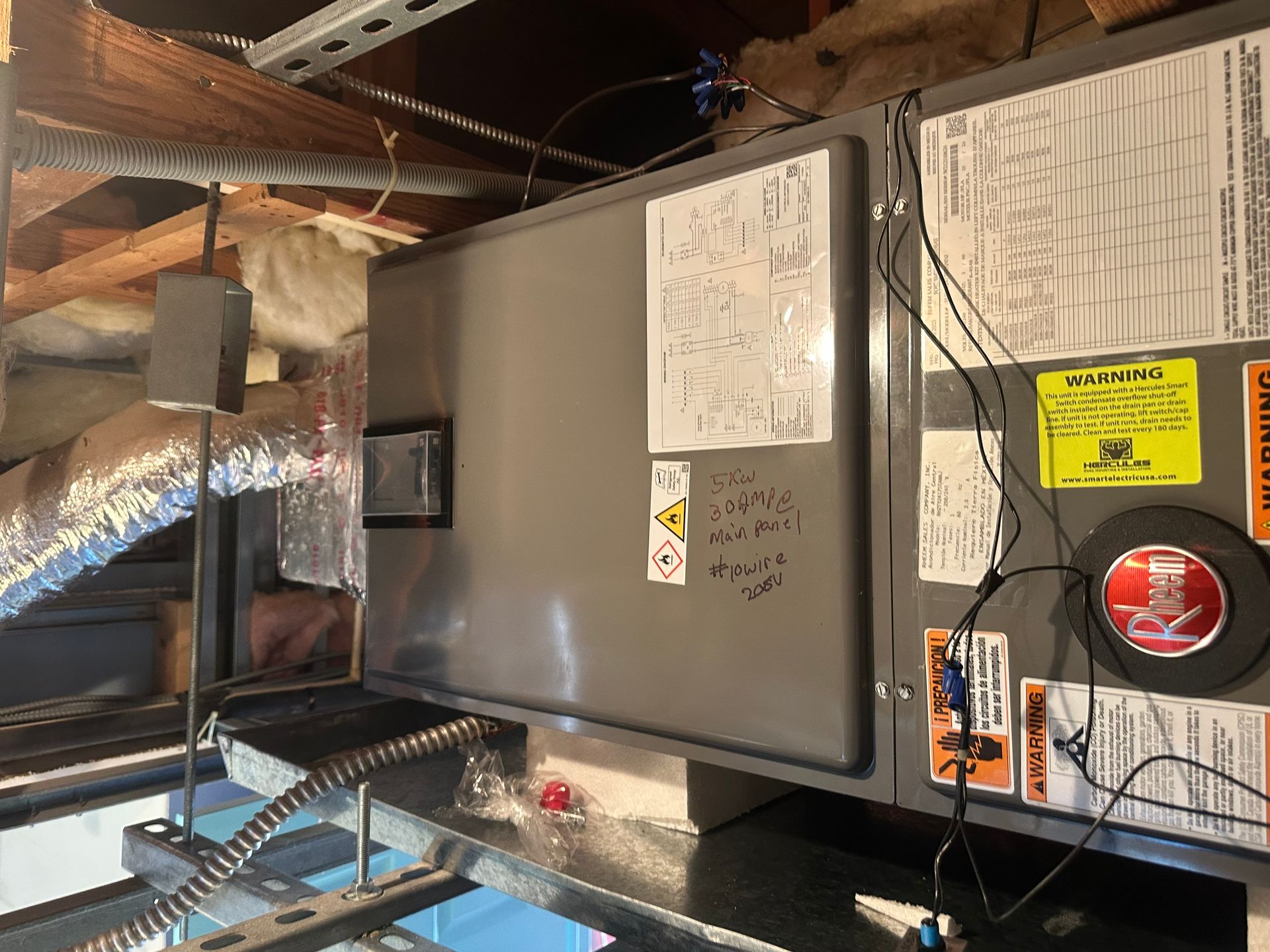HVAC unit in an attic with ductwork, electrical wires, and warning labels.