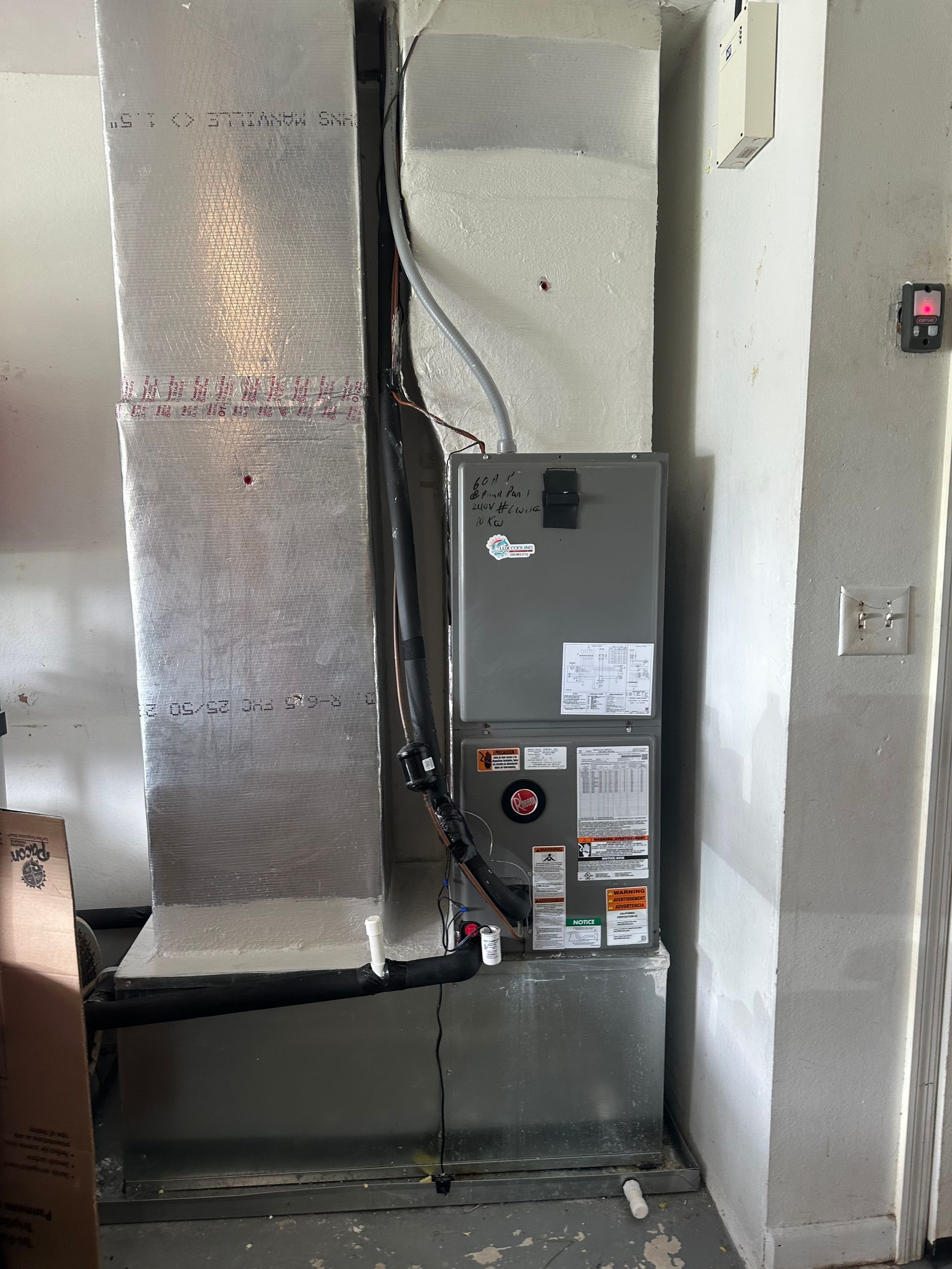 Furnace unit with ductwork in a room with a light switch and electrical outlet on the wall.