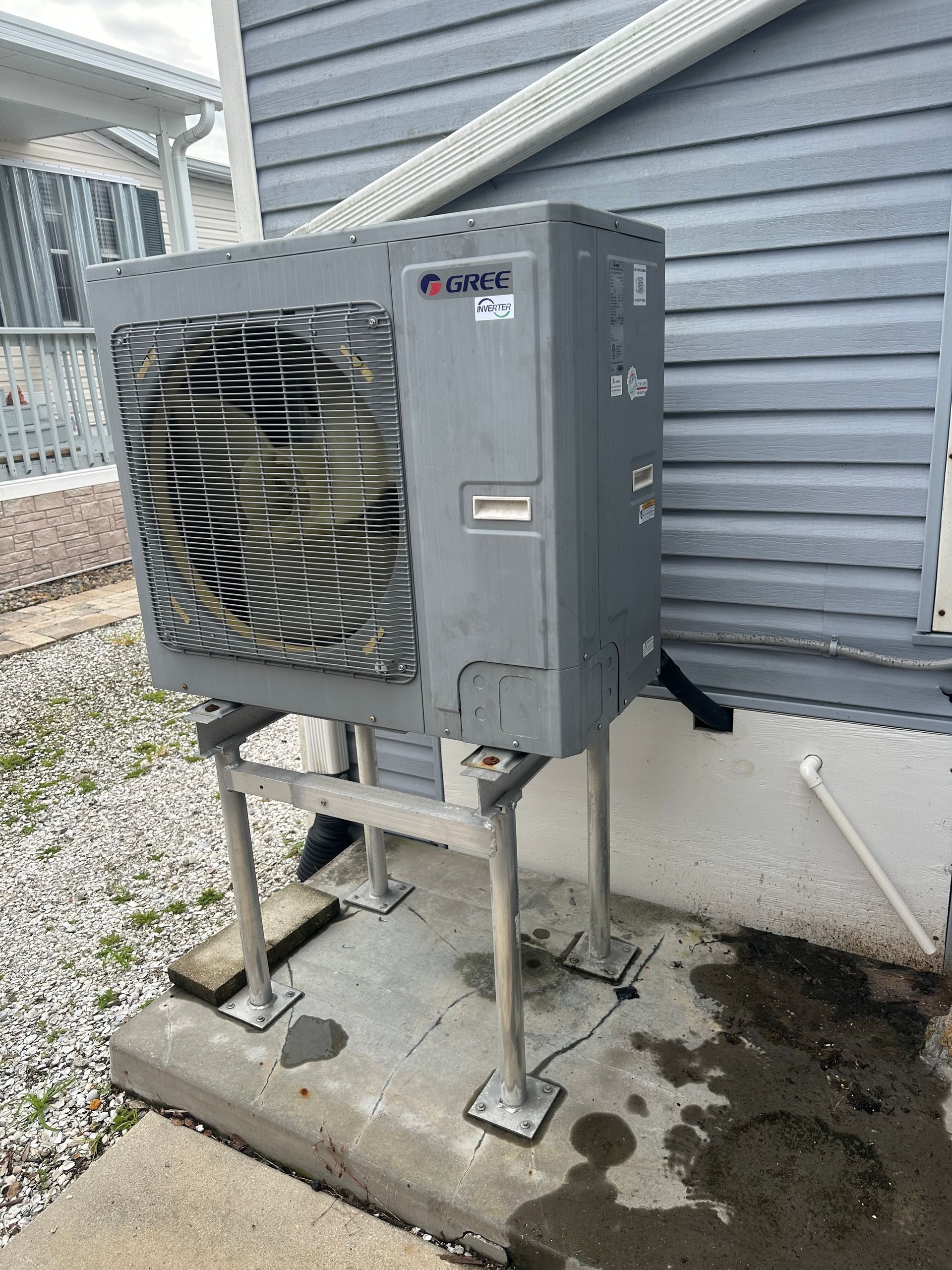 Gray HVAC unit, mounted on metal supports outside a building with white siding.