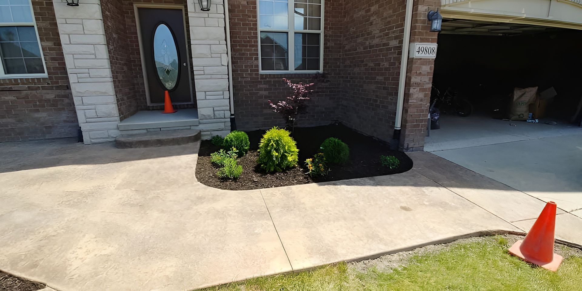A house with a concrete walkway, garden bed, and orange safety cones.