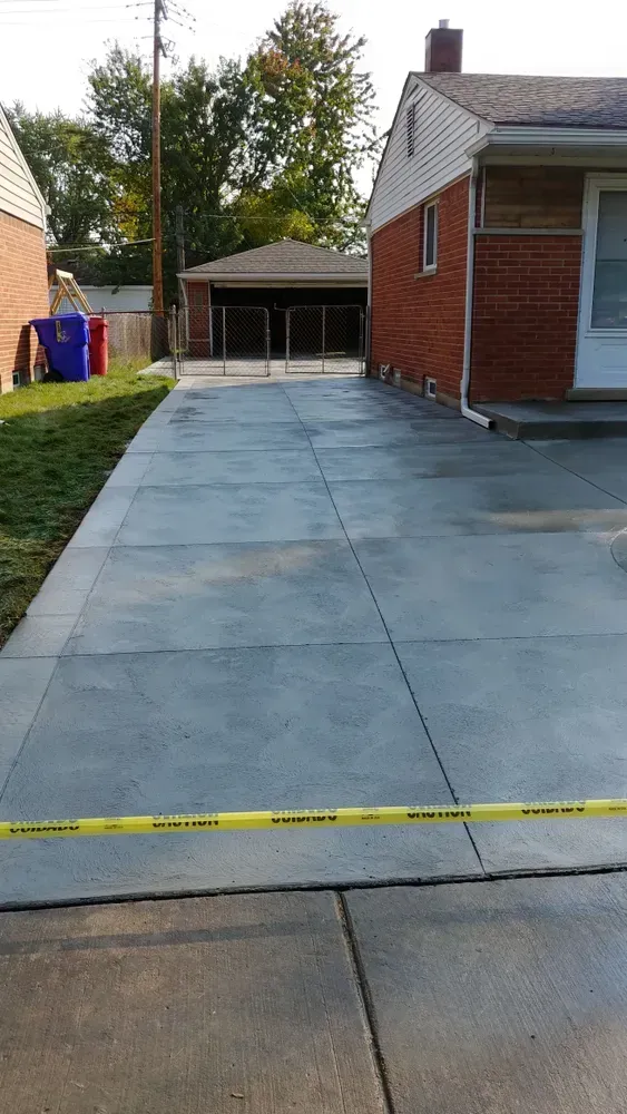 New concrete driveway with caution tape, next to a red brick house and grass.