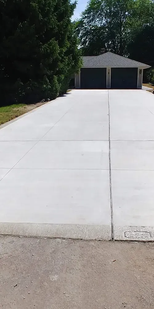 Concrete driveway leading to a two-car garage with dark gray doors, surrounded by green trees.