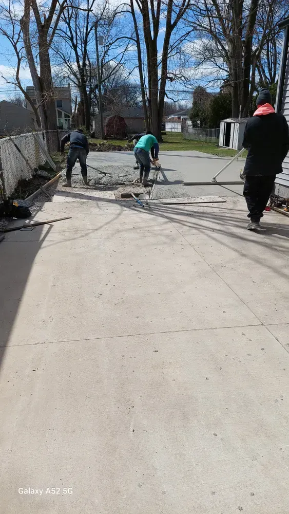 Three workers leveling concrete on a driveway; sunny day.