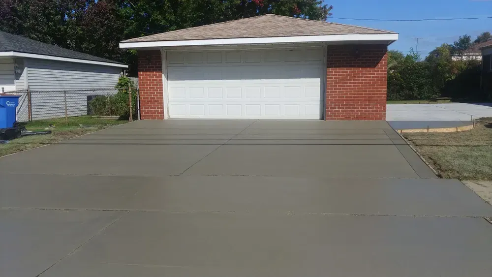 Freshly poured concrete driveway in front of a red brick garage with a white garage door.