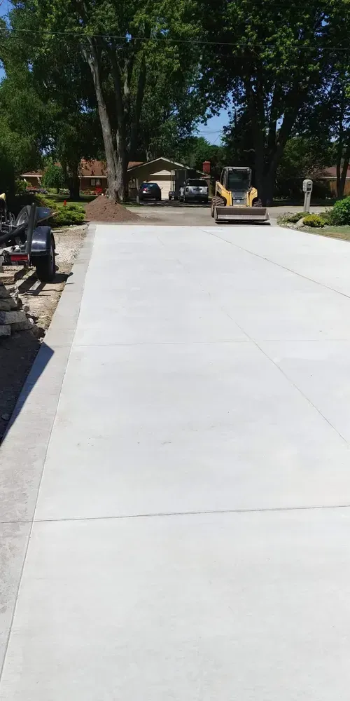 Newly poured concrete driveway with heavy machinery in residential setting.