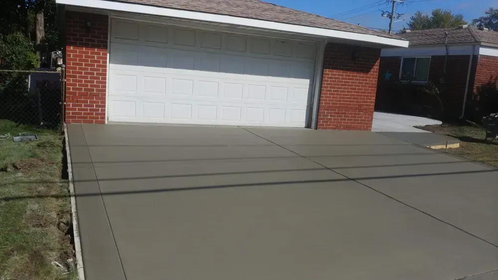 Freshly poured concrete driveway in front of a garage with a white door.