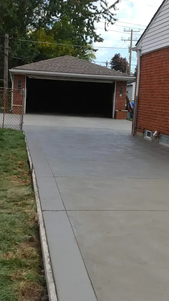 New concrete driveway leading to a brick garage; green grass borders the left side.