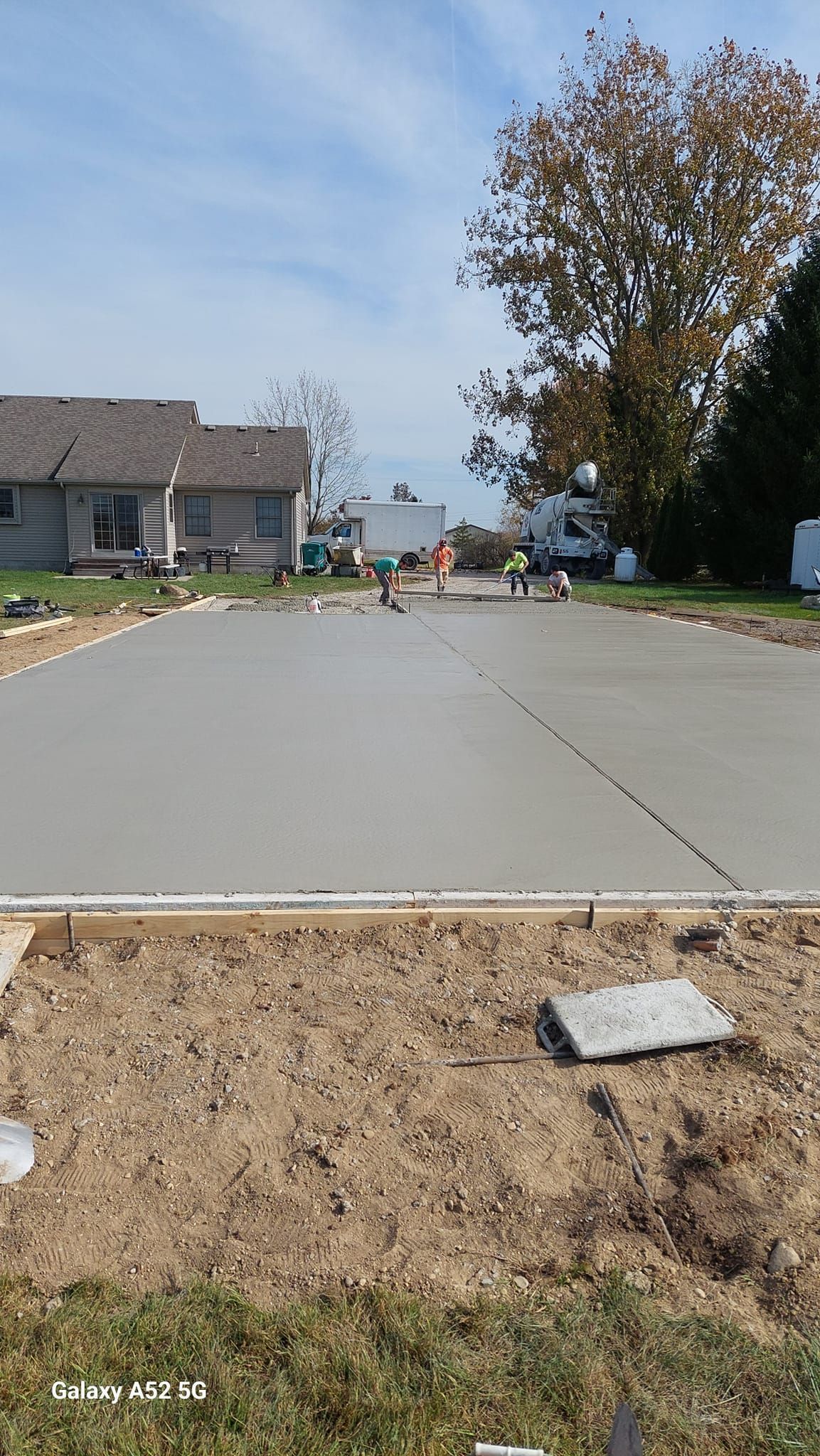 New concrete being poured for a driveway; workers in orange vests, houses in the background, sunny day.