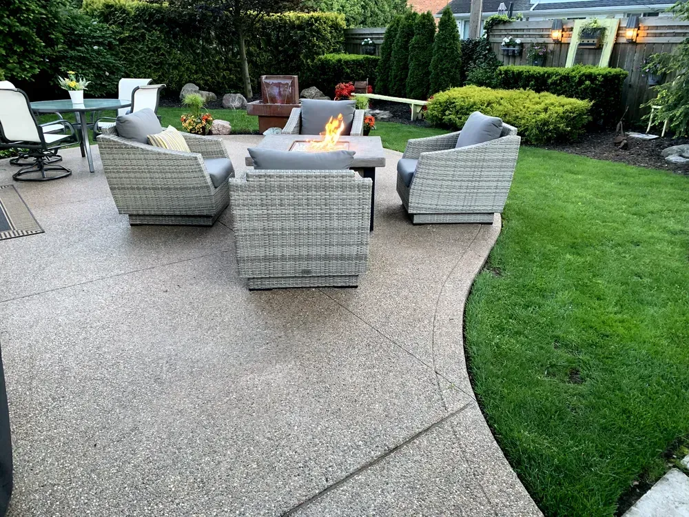 Outdoor patio with gray wicker furniture, fire pit, and green grass.