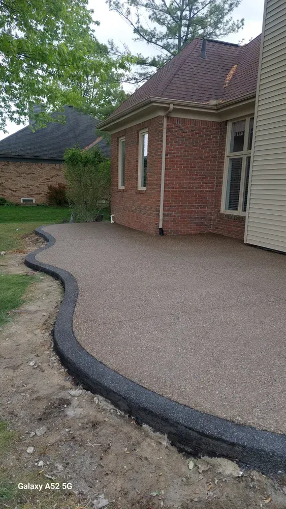 Concrete patio with curved black border next to a brick house, on a cloudy day.