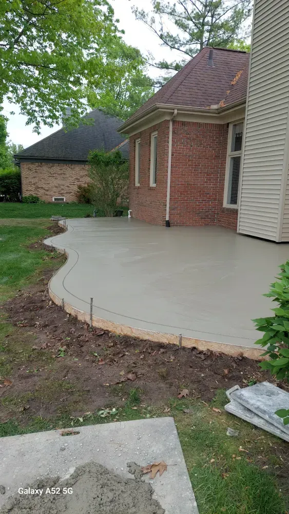 A newly poured concrete patio next to a brick house, with a curved border.