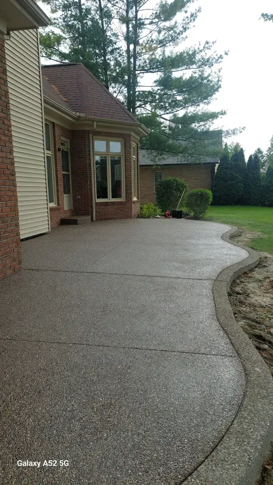 A concrete patio with a curved edge next to a brick house and green lawn.