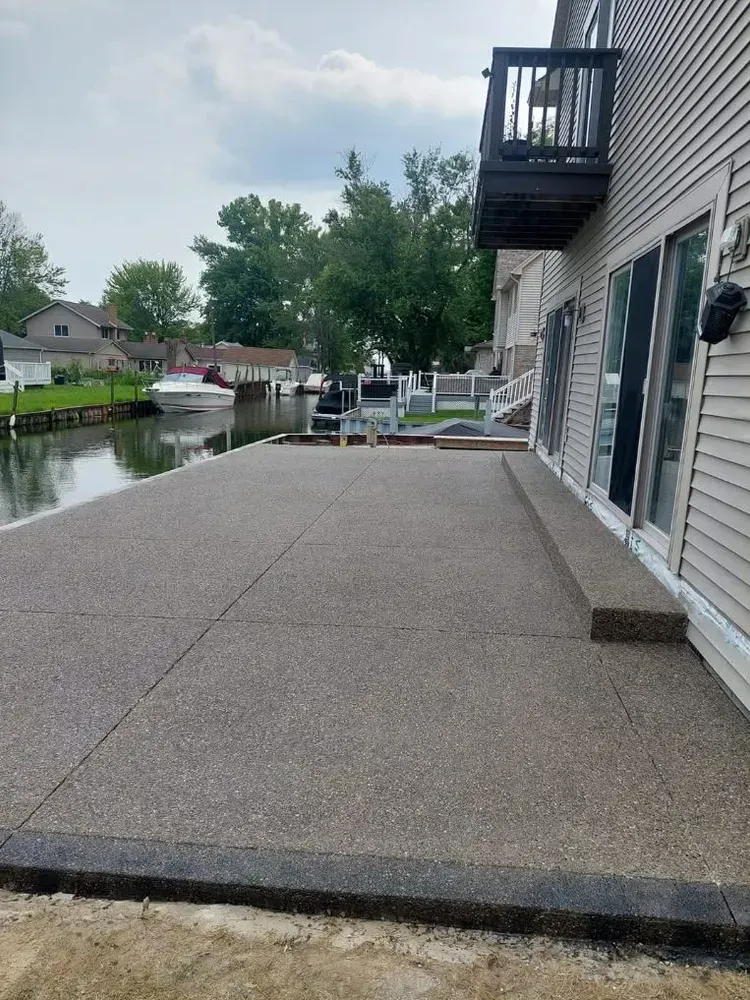 Concrete patio next to a house with a balcony and water view.