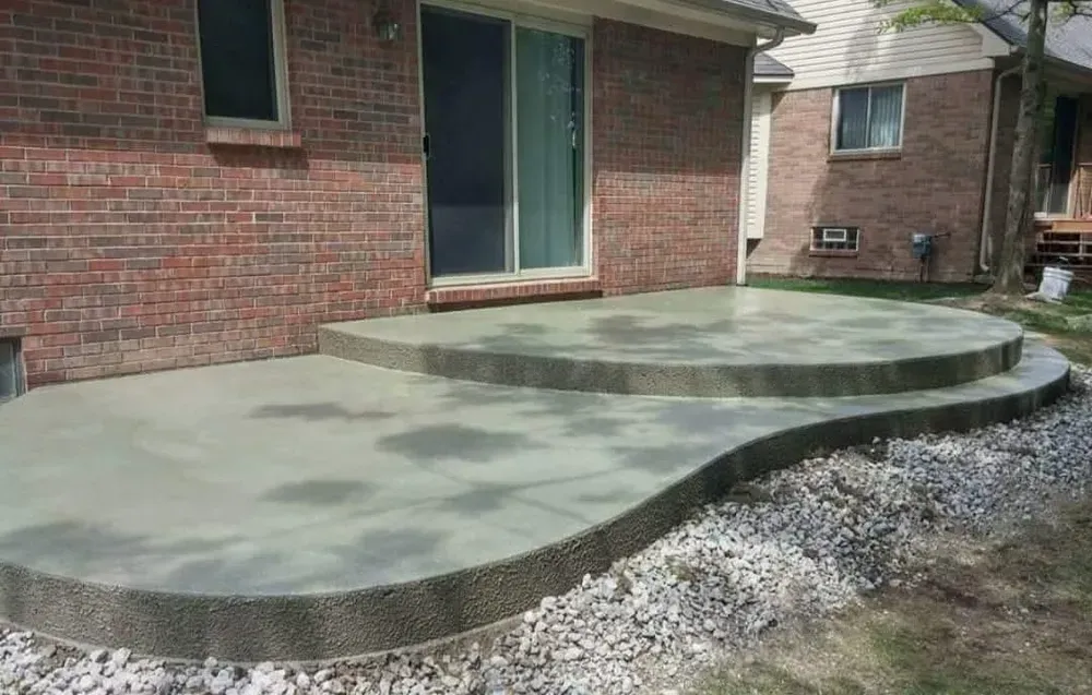 Concrete patio with two levels, steps, next to brick house and grassy yard.