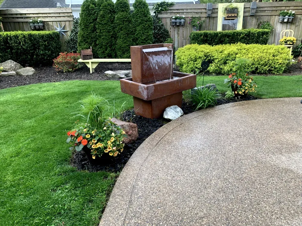 A decorative outdoor water fountain in a well-landscaped backyard with green grass and shrubs.